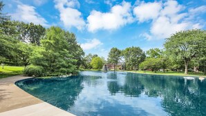 A swimming pool with a fountain, surrounded by trees and a clear sky.