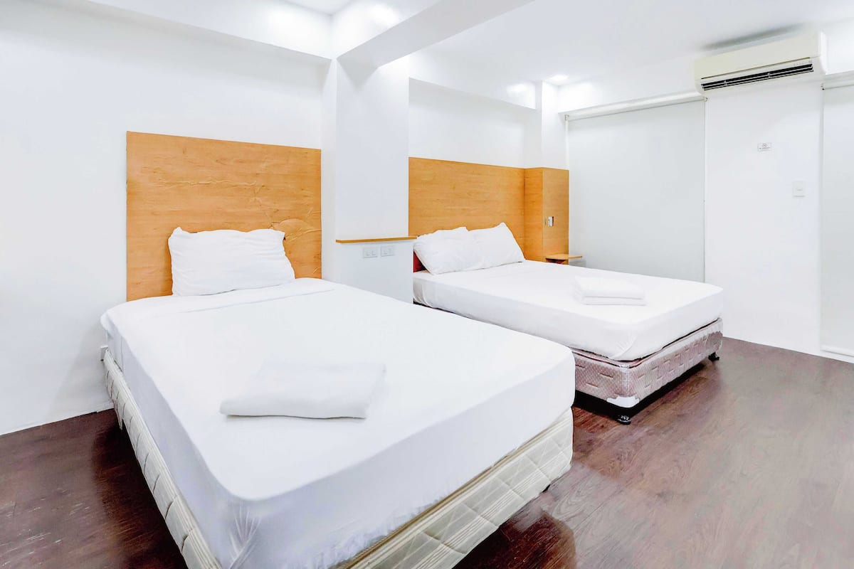 Habitación de hotel con dos camas, cabeceros de madera, ropa de cama blanca y un armario.