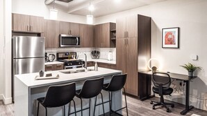 A modern kitchen with stainless steel appliances, a central island with bar stools, and a dining area with a desk and chair.