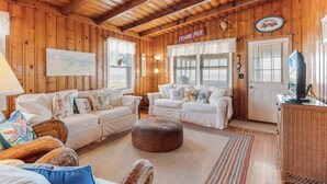 A cozy cabin interior with wooden walls, two white sofas, a brown ottoman, and a wicker side table.