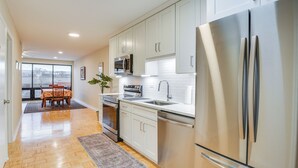 A modern kitchen with stainless steel appliances, white cabinetry, and a dining area with a table and chairs. - Steps to Shops & Eats: Apt in Portage Park! (Chicago)
