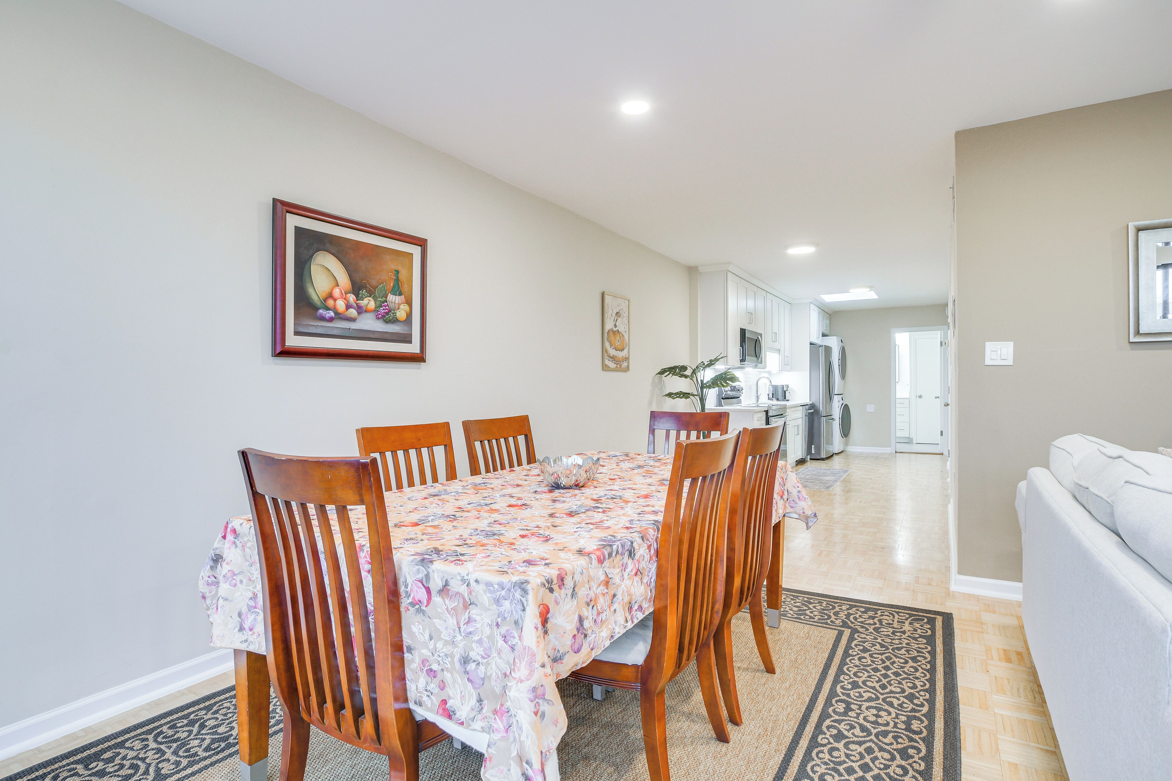A dining area with a table and chairs, a kitchen in the background, and a living room with a couch.