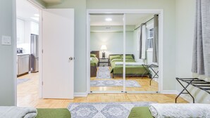 A modern bedroom with a sliding glass door leading to a bathroom, a bed with green bedding, and a small bedside table with a lamp. - Steps to Shops & Eats: Apt in Portage Park! (Chicago)
