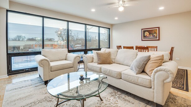 A spacious living room with a large window, a glass coffee table, and a beige sofa. - Steps to Shops & Eats: Apt in Portage Park! (Chicago)