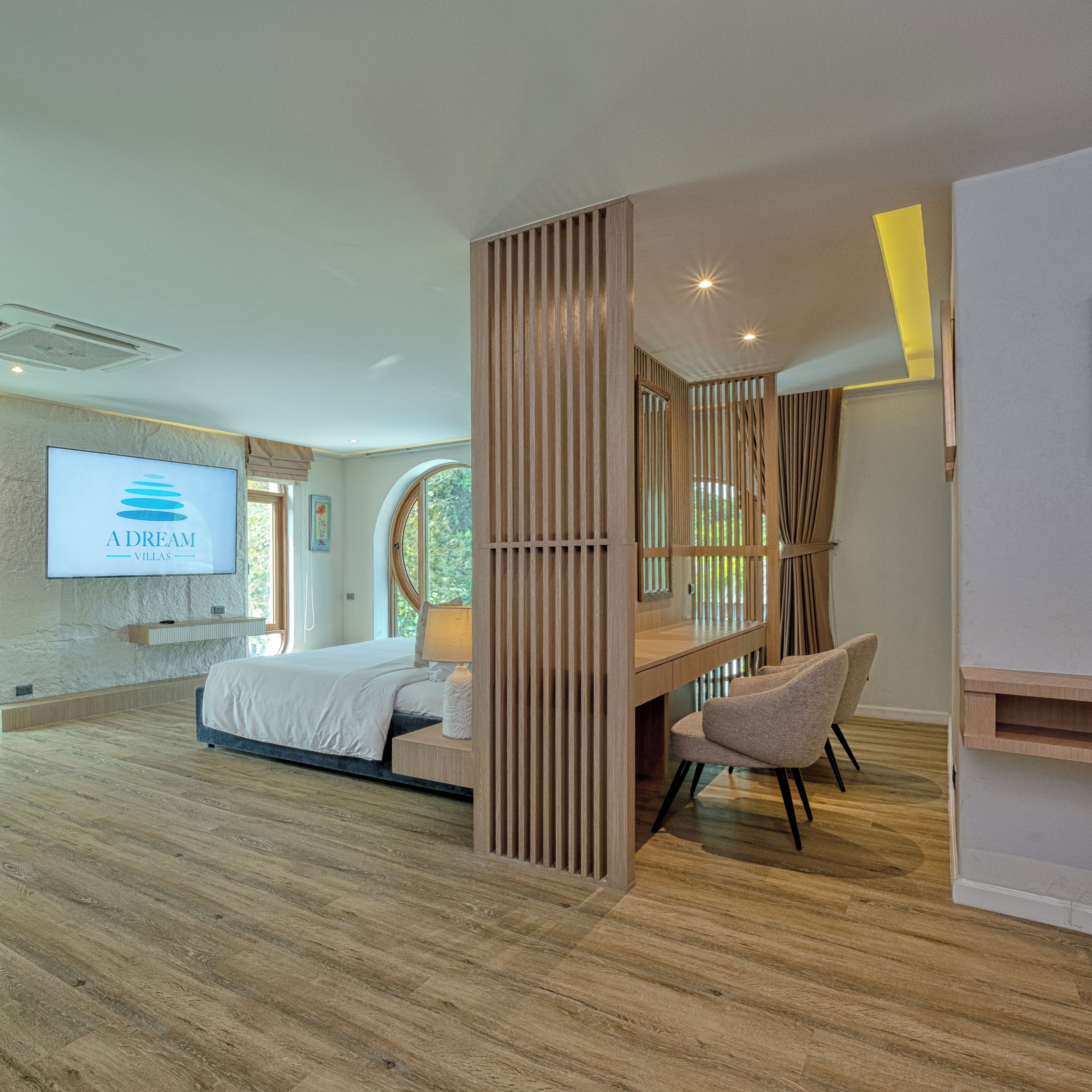 A modern bedroom with a bed, a desk, and a chair. There is a TV mounted on the wall displaying 'A Dream Villas'.