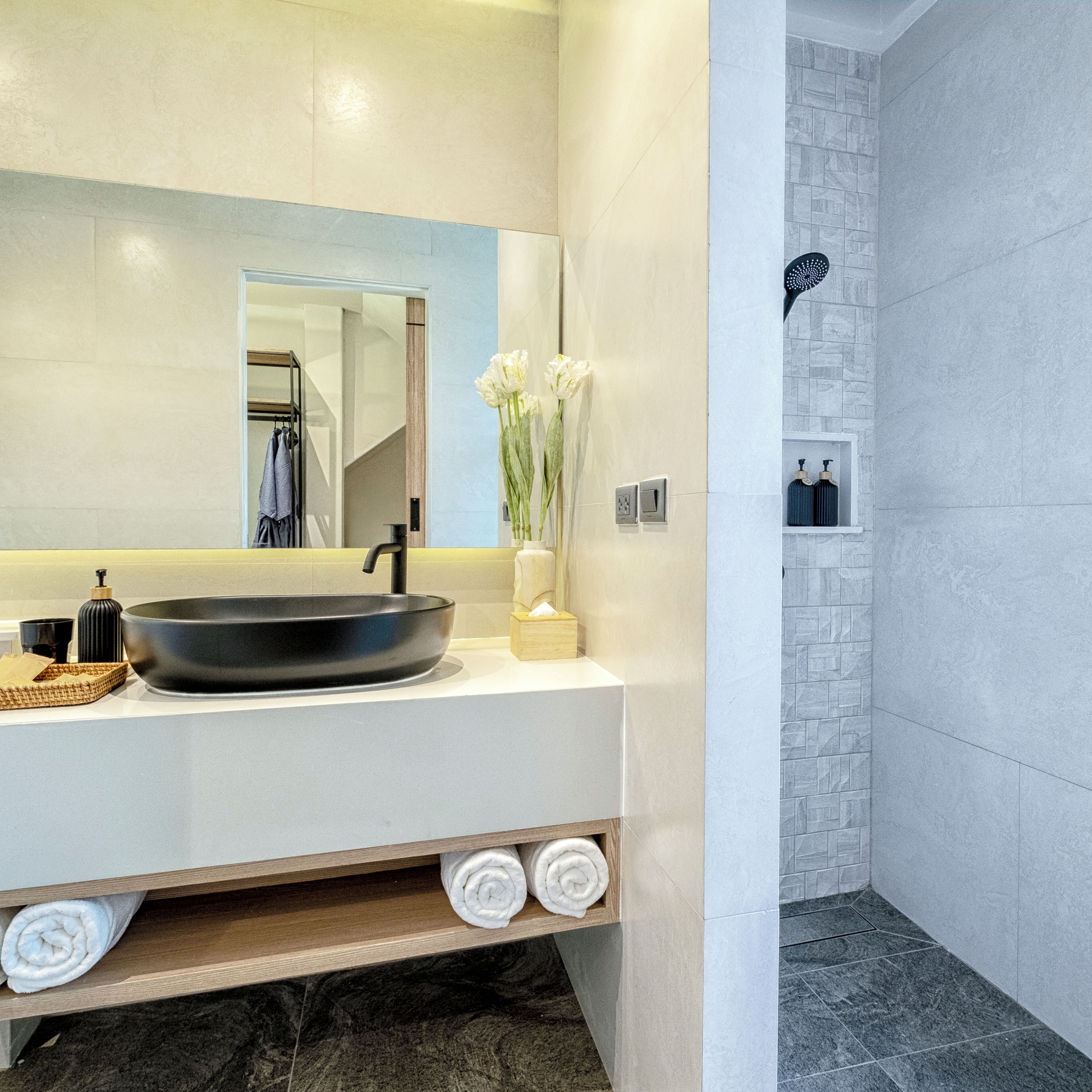 A modern bathroom with a large mirror, black sink, white towels, and a shower area.