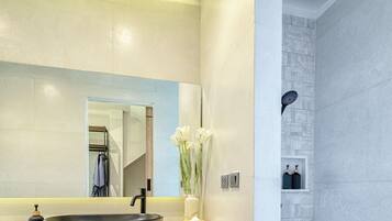 A modern bathroom with a large mirror, black sink, white towels, and a shower area.