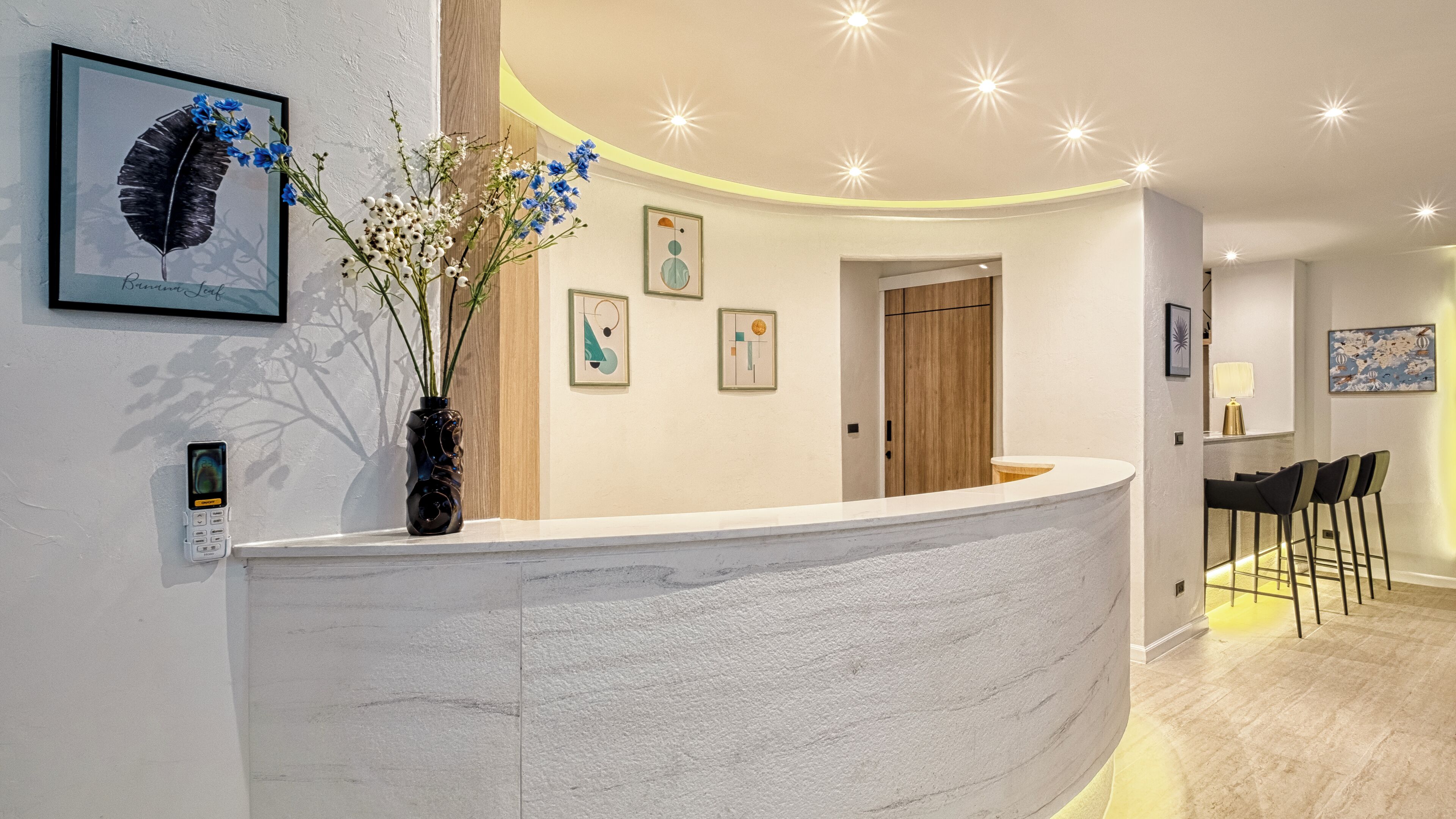 A modern reception area with a curved reception desk, framed artwork on the walls, and a wooden door in the background.