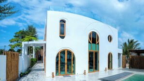 Una casa moderna con amplios ventanales arqueados, un porche cubierto y fachada blanca.