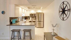 A modern kitchen with white cabinets, stainless steel appliances, and a central island with stools. - 8 Mi to Beach: Modern Condo in Fort Myers! (Fort Myers)