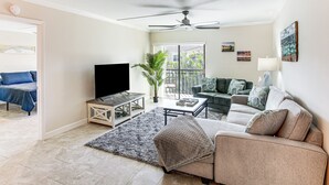 A living room with a flat-screen TV, a ceiling fan, a sofa, a coffee table, and a potted plant. - 8 Mi to Beach: Modern Condo in Fort Myers! (Fort Myers)