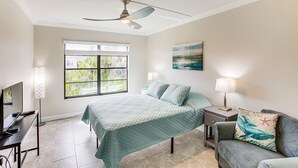 A bedroom with a bed, a desk, a chair, a TV, a ceiling fan, a window, and a painting on the wall. - 8 Mi to Beach: Modern Condo in Fort Myers! (Fort Myers)