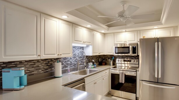 A modern kitchen with white cabinets, stainless steel appliances, and a blue coffee maker. - 8 Mi to Beach: Modern Condo in Fort Myers! (Fort Myers)