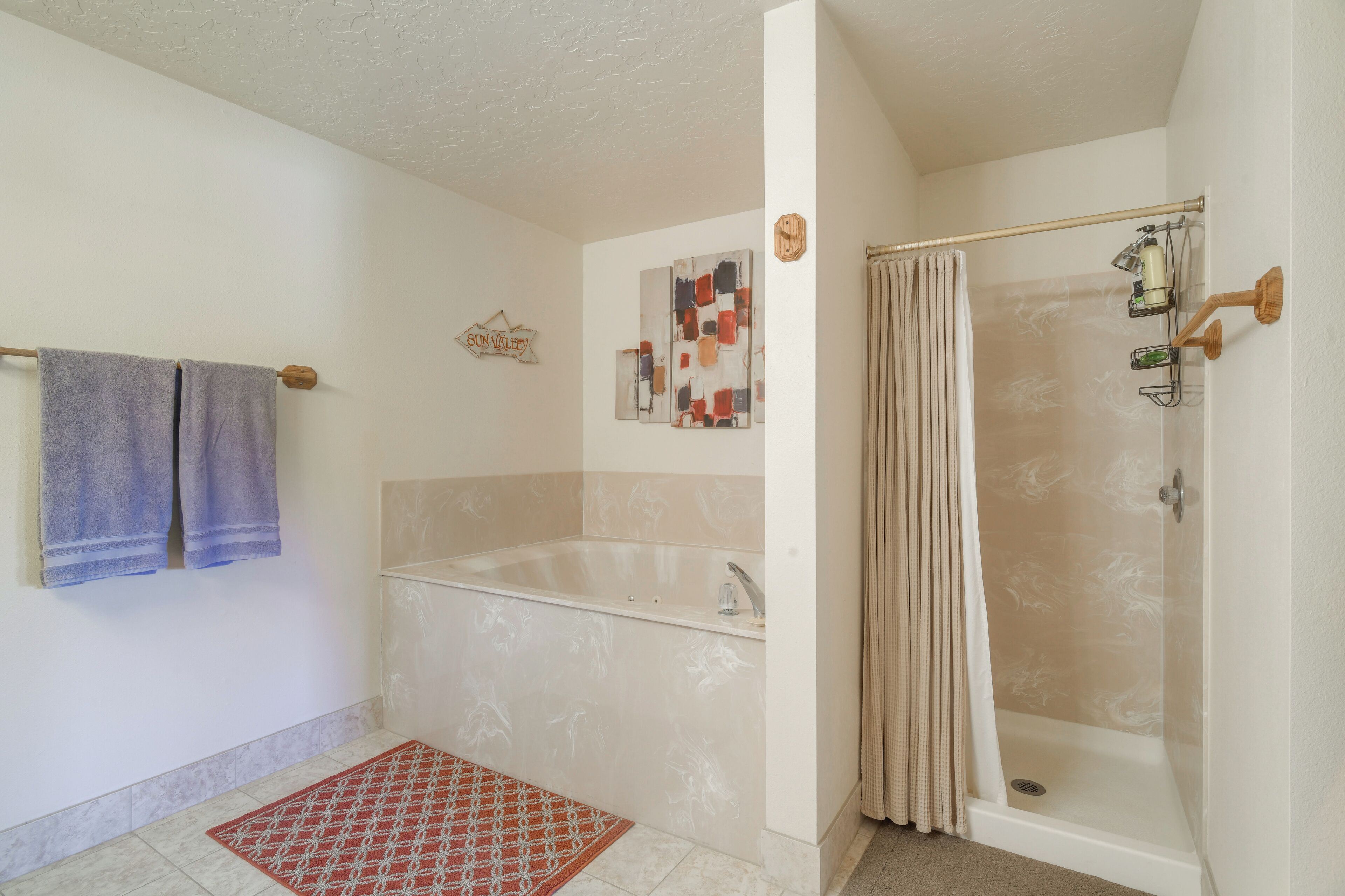 A bathroom with a bathtub, shower, and a red patterned rug.