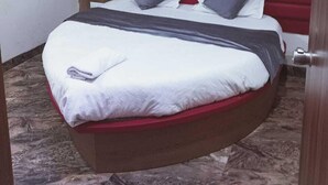 A hotel room with a curved bed, a red heart decoration on the wall, and a ceiling fan.
