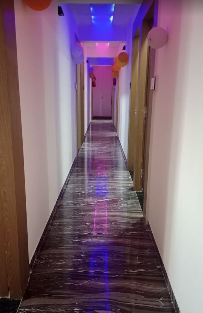 A hallway with a glossy black floor, white walls, and a ceiling with blue and purple lighting.