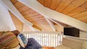 A cozy attic bedroom with a wooden ceiling, a bed with patterned pillows, a sofa, and a TV mounted on the wall. - < 1 Mi to Beech Mtn! All-Season Outdoor Retreat (Beech Mountain)