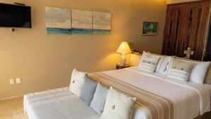 A hotel room with a large bed, a bedside table with a lamp, a TV mounted on the wall, and artwork on the walls.
