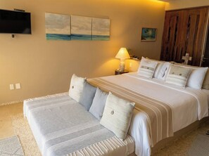Une chambre d’hôtel avec un grand lit, une table de chevet avec une lampe, un téléviseur fixé au mur et des œuvres d’art accrochées aux murs.