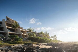 Un hôtel situé en bord de mer, doté de nombreux balcons, de palmiers et d’une côte rocheuse.