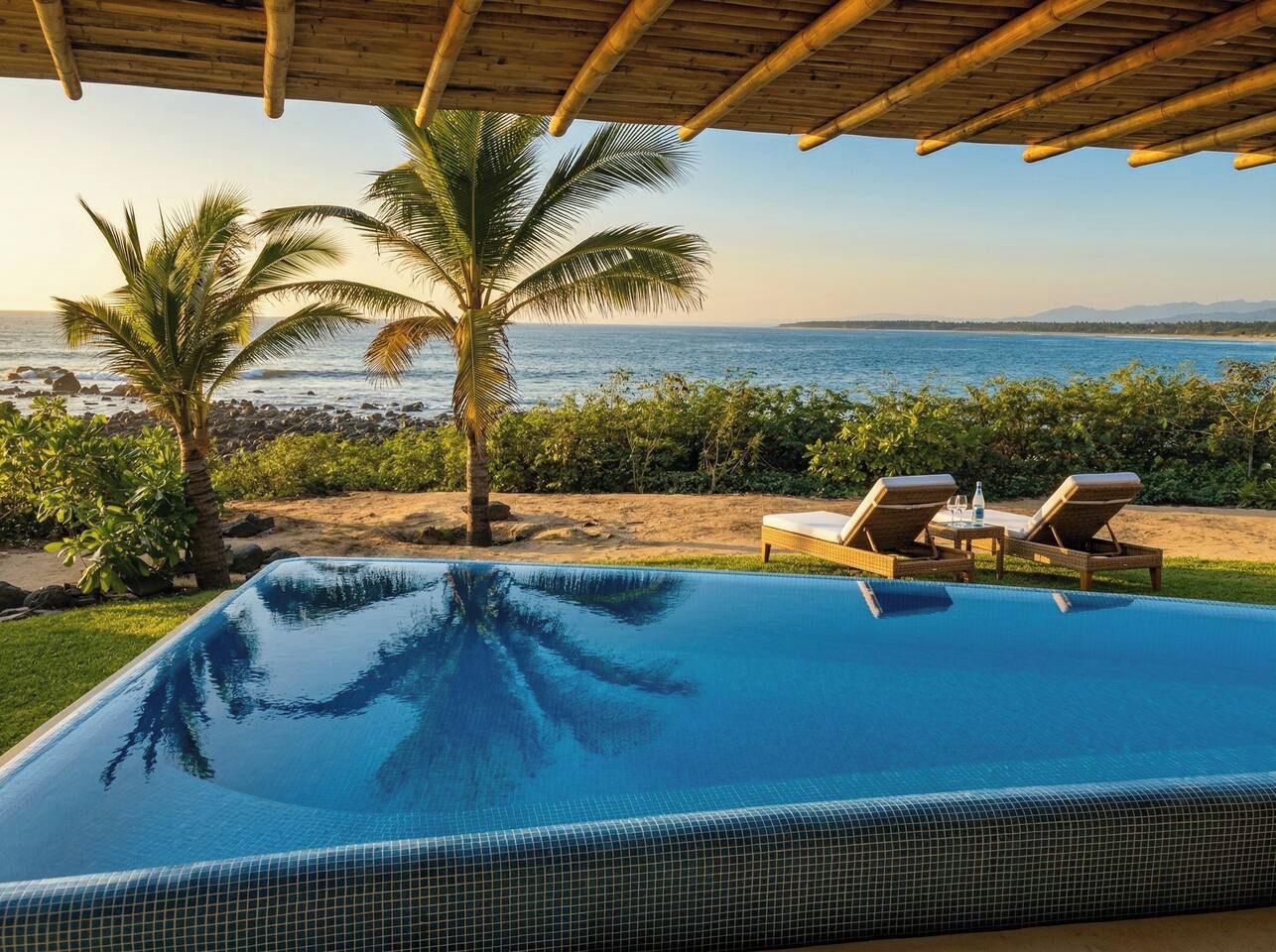 A swimming pool with a view of the sea, palm trees, and lounge chairs.