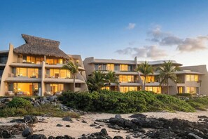 Un hotel sulla spiaggia con numerosi balconi, palme e una struttura con tetto di paglia.