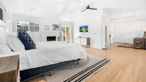 Ein modernes Schlafzimmer mit einem großen Bett, einem Kamin, einem Schreibtisch und Blick ins Freie.