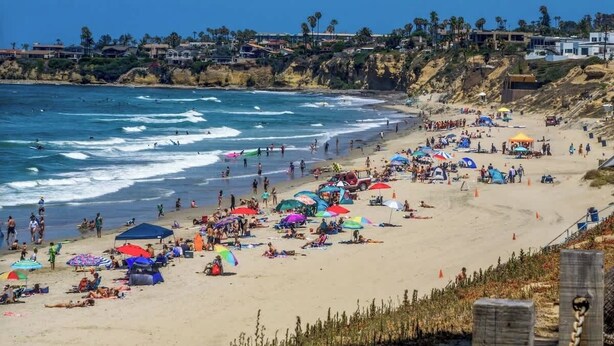 Ein belebter Strand voller Menschen, Sonnenschirme und Liegestühle.