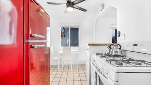 Una cocina con un refrigerador rojo, armarios blancos, una estufa a gas y un ventilador de techo.
