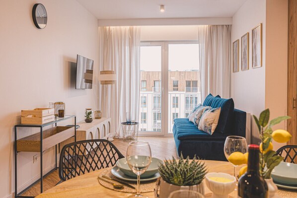 A modern living room with a sofa, dining table, and a TV mounted on the wall.