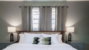 Una cama bien hecha con sábanas blancas, una almohada decorativa y dos lámparas de noche en mesitas a juego.