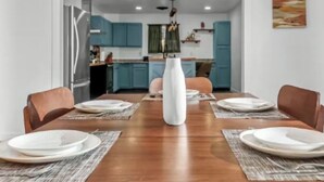 Un comedor con una mesa de madera dispuesta para cuatro, un jarrón blanco como centro de mesa y armarios azules al fondo.