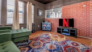 Una sala de estar moderna con un sofá verde, un tapete estampado, un televisor en una pared de ladrillo y una mesa de centro de madera.