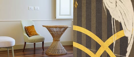 Une pièce comprenant un fauteuil de couleur claire, une table d’appoint en osier et deux œuvres d’art encadrées accrochées au mur.