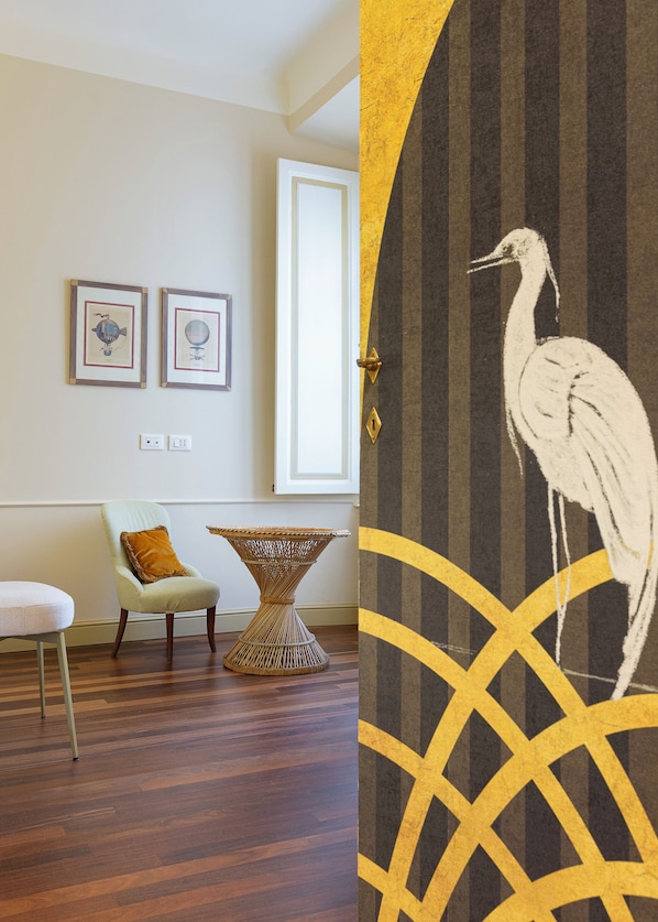 A room with a light-colored armchair, a wicker side table, and two framed artworks on the wall.