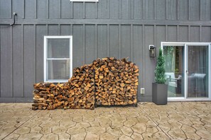 A building exterior with a grey siding, a stack of firewood, a window, and a door with a glass panel. - 6BR Poconos Retreat, Hot Tub, Game Room, Fire Pit (Blakeslee)