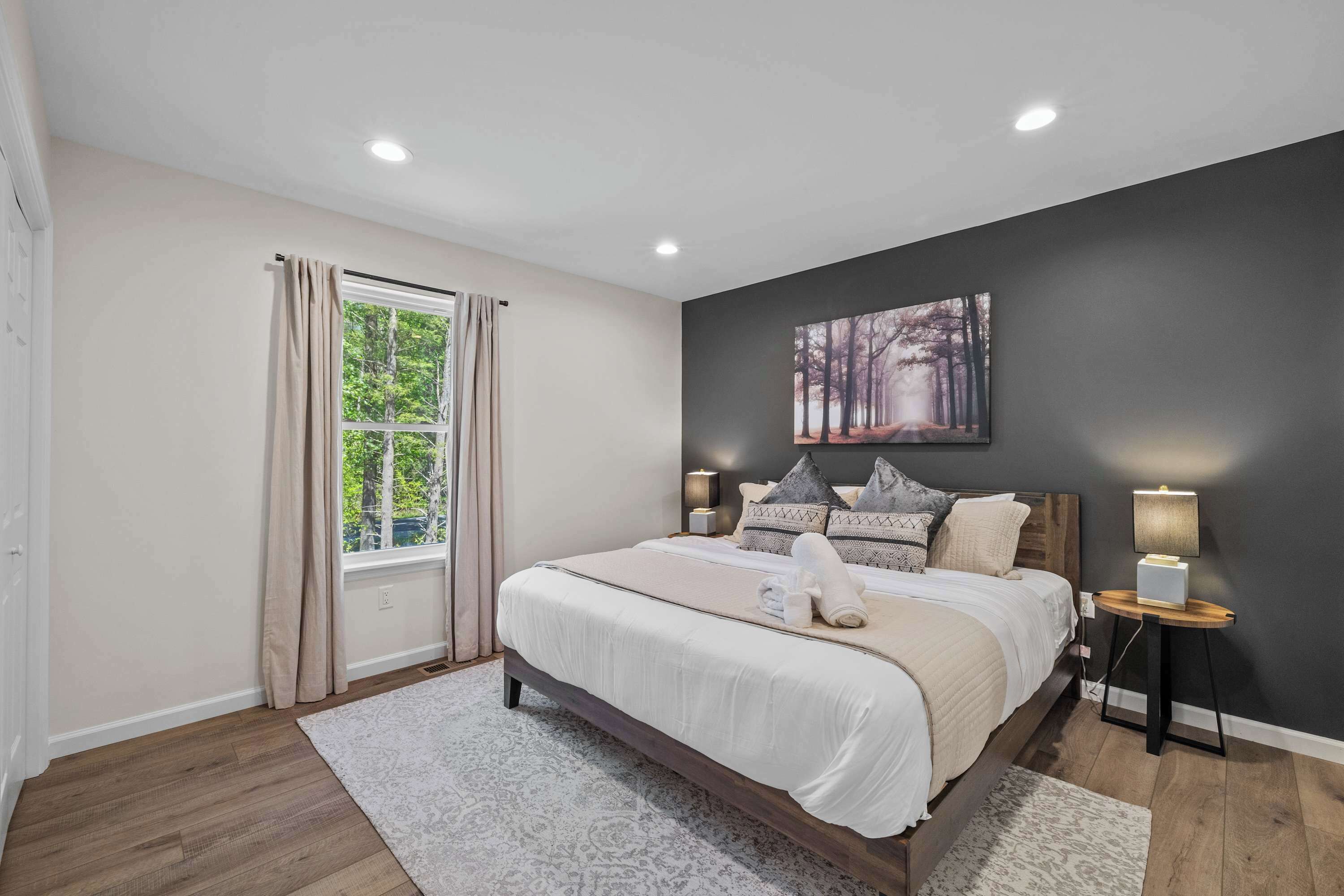 Une chambre à coucher avec un grand lit, une fenêtre avec des rideaux, une table de chevet avec une lampe et un tableau accroché au mur.
