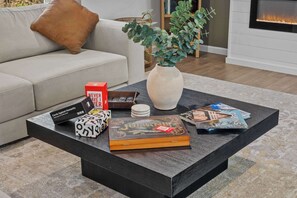 A modern living room with a dark coffee table, a beige sofa, a vase with green plants, and a fireplace. - 6BR Poconos Retreat, Hot Tub, Game Room, Fire Pit (Blakeslee)