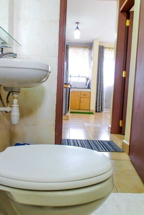 Ein Badezimmer mit Toilette, Waschbecken und einem sichtbaren Küchenbereich im Hintergrund.