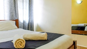 Een hotelkamer met een bed, een opgerolde handdoek en een spiegel aan de muur.