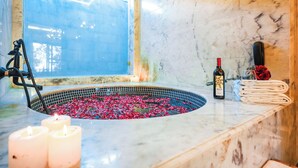 A bathroom with a circular hot tub filled with rose petals, a bottle of Sula wine, glasses, and towels on a marble countertop. - Estherea Resort and Spa, Jaipur (Bassi)