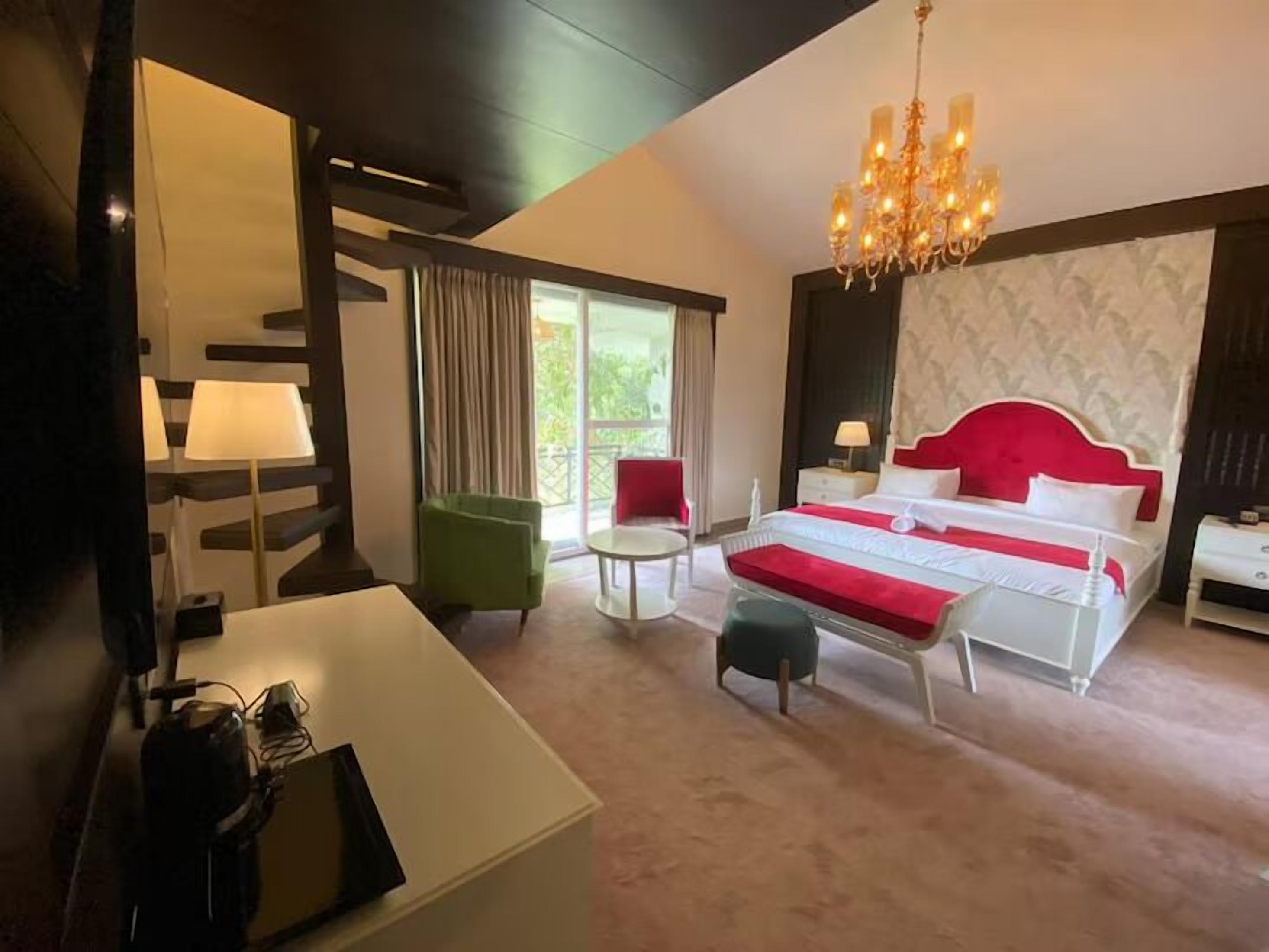 Une chambre d’hôtel avec un grand lit, un bureau, une chaise, un lustre et une vue sur la verdure.