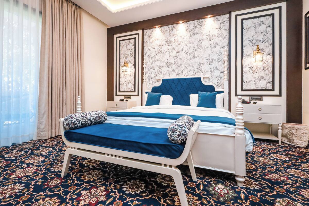 A bedroom with a large bed, a nightstand, a dresser, and a patterned carpet.