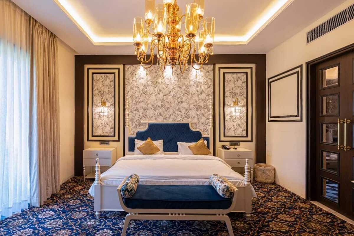 A luxurious bedroom with a large bed, ornate chandelier, and patterned wallpaper.
