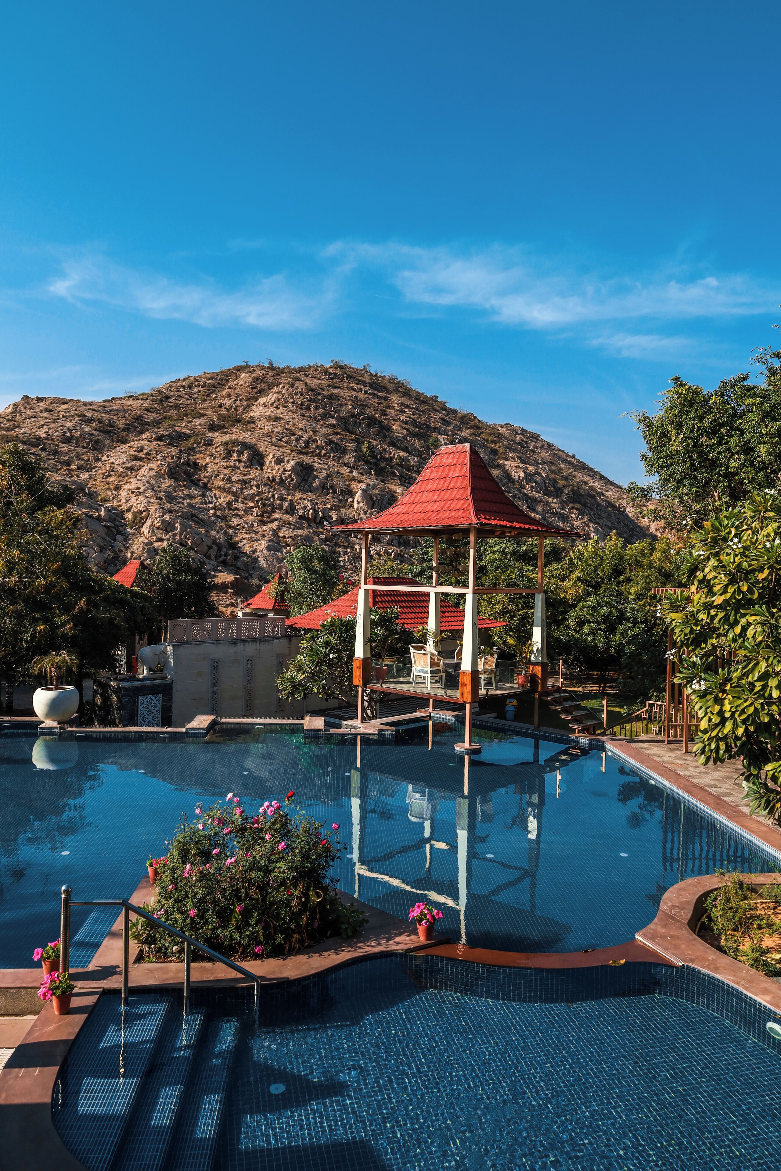 A swimming pool with a gazebo, surrounded by greenery and a mountainous backdrop.