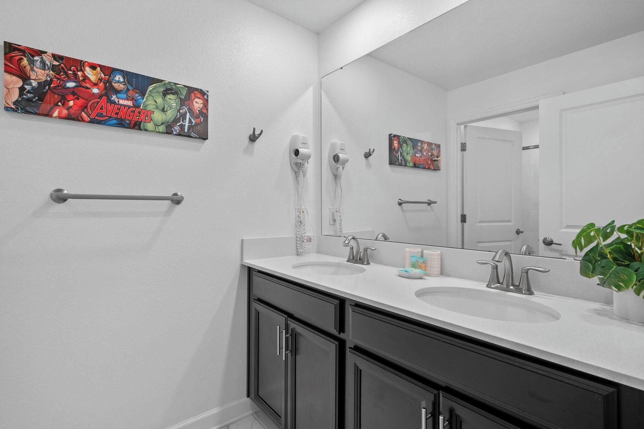 A modern bathroom with two sinks, a large mirror, and a wall-mounted hairdryer.