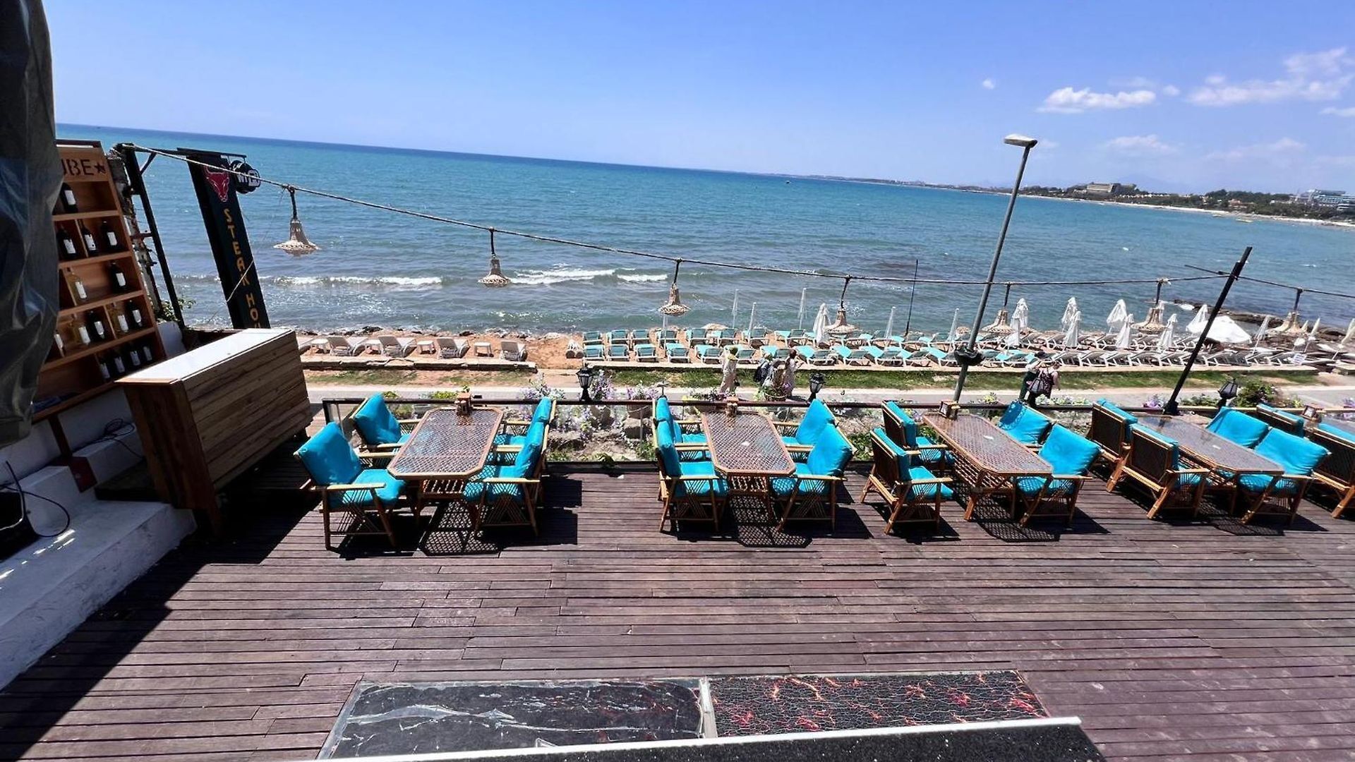 A wooden deck with outdoor seating, overlooking a beach with lounge chairs and umbrellas.