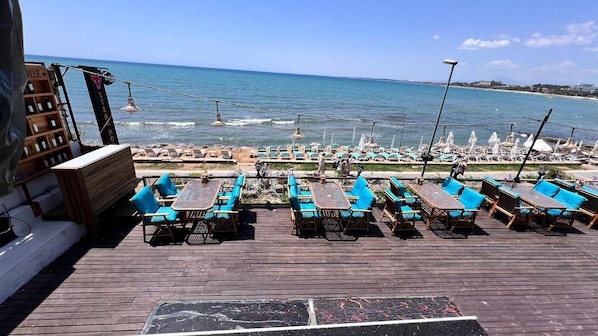A wooden deck with outdoor seating, overlooking a beach with lounge chairs and umbrellas. - Cuba Beach Hotel (Manavgat)