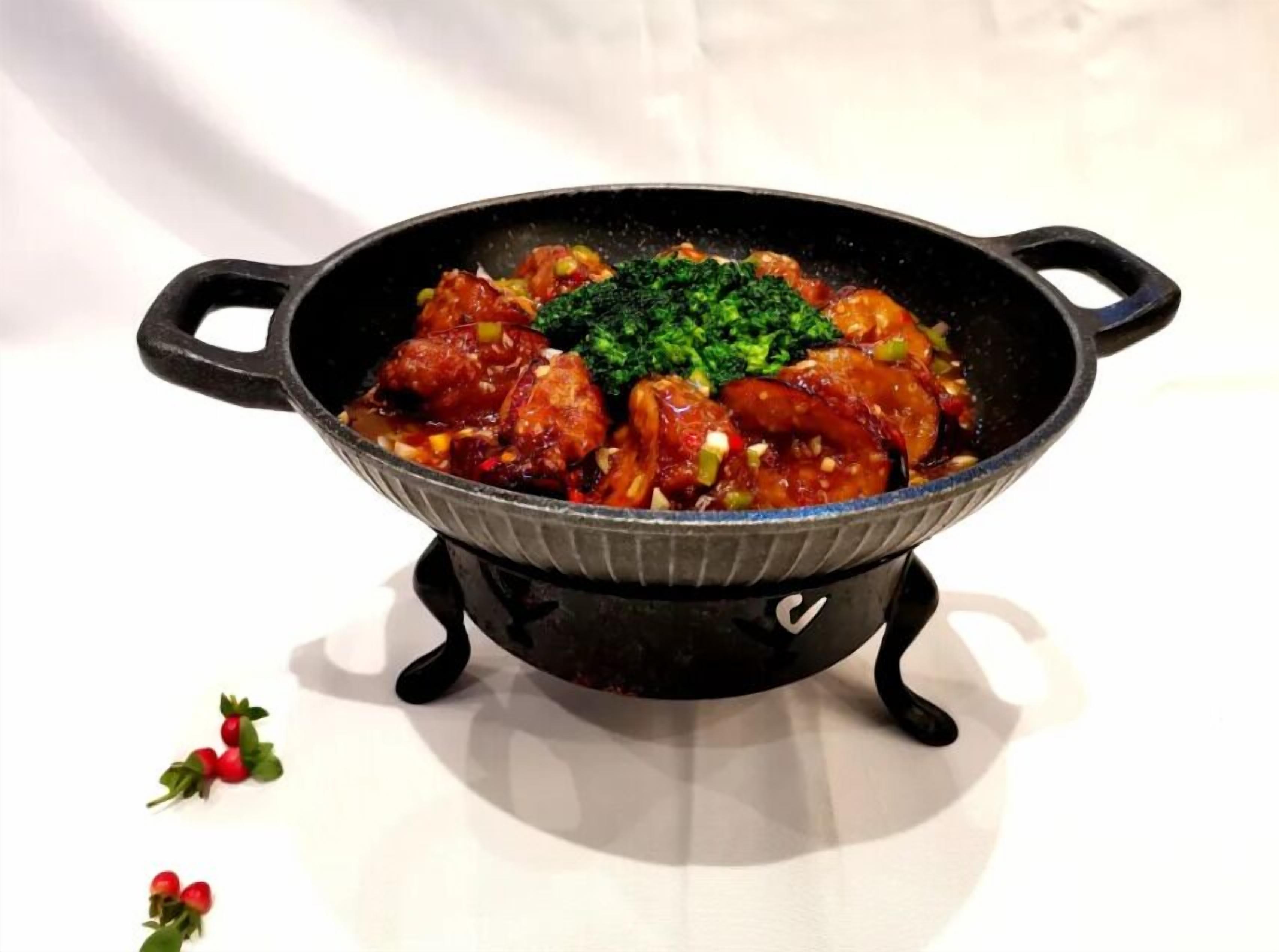 A black cast iron skillet with handles, containing a dish with meat and broccoli, placed on a white surface.