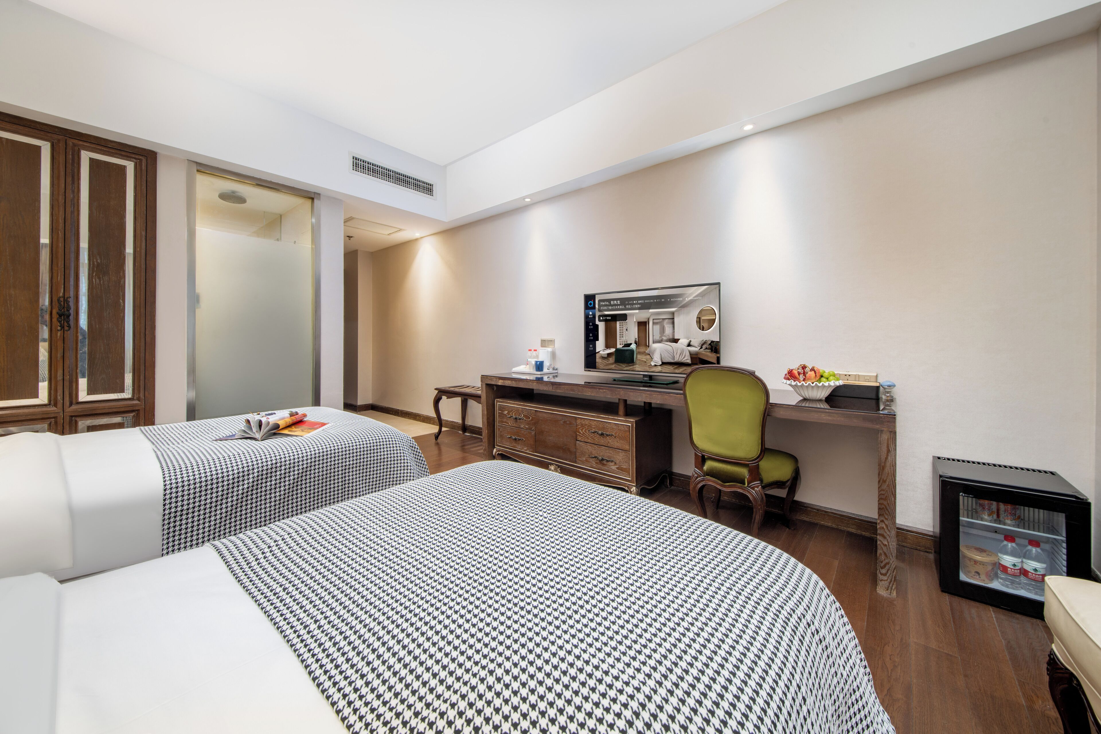 A hotel room with two beds, a desk, a chair, a mirror, and a minibar.